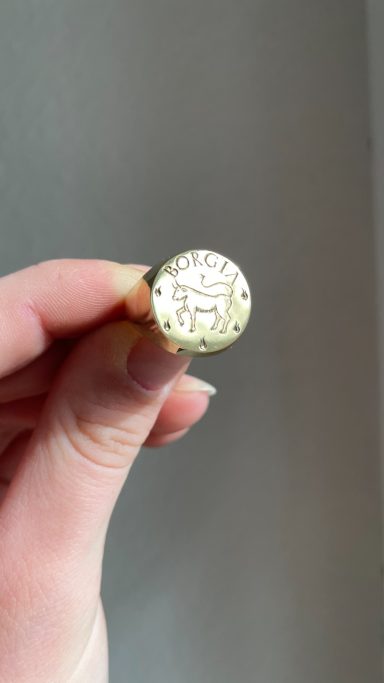 Eine Person hält einen goldenen Stift mit eingeprägtem Design in der Hand.