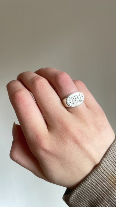 Eine Hand mit einem ovalen, weißen Ring auf einem neutralen Hintergrund.