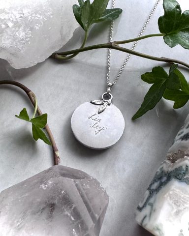 Silberne Kette mit Anhänger und gravierter Schrift, umgeben von transparenten Kristallen.